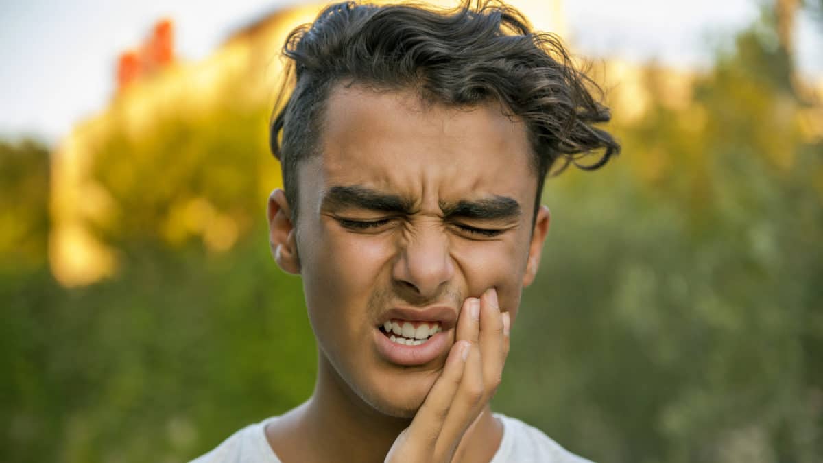 Young man holding face in pain Washington MI dentist